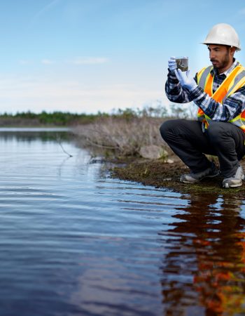 Portait of a professional scientist with protective gear examining the marsh lands in Canada and taking sample of marine plant life for research